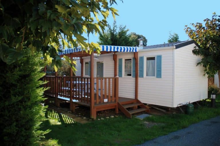Mobil-home avec terrasse en bois et auvent rayé.