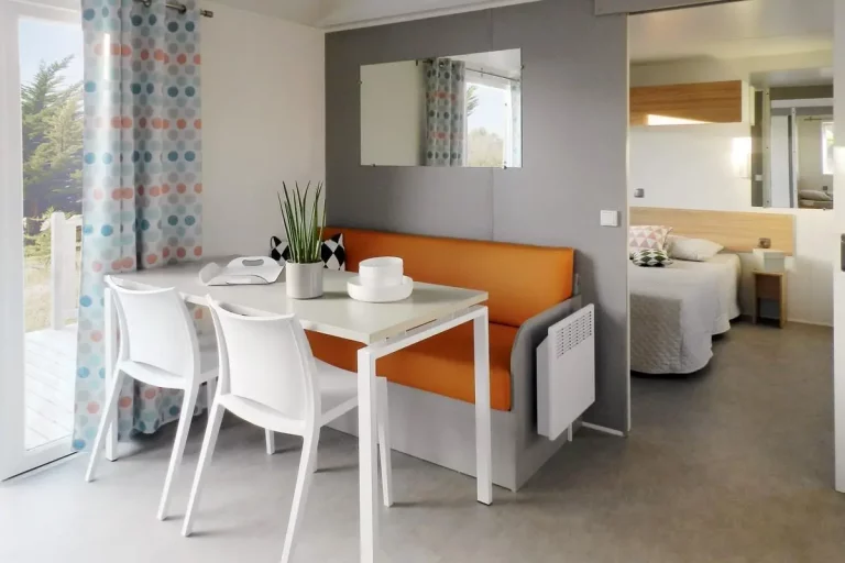 Séjour d'un mobil-home au camping La Frétille : table, banquette et chambre avec lit double en arrière-plan