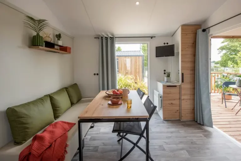 Séjour d'un mobil-home avec télévision murale, banquette et porte-fenêtre ouverte sur la terrasse